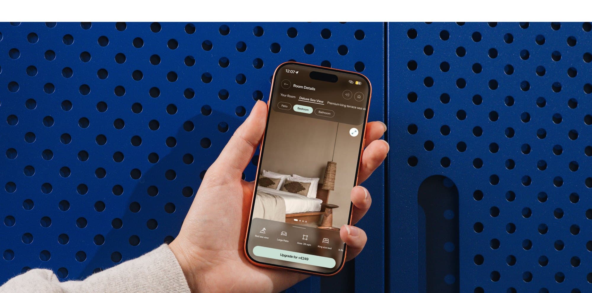 A guest holding an iPhone showing the redesigned Genie pre-arrival room screen